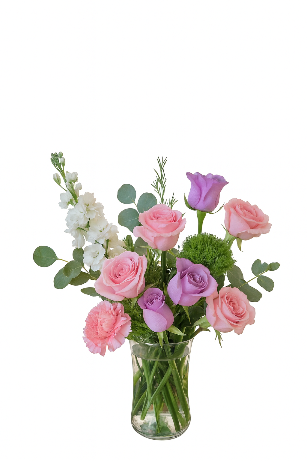 This elegant floral arrangement is set in a clear glass vase and features a graceful blend of soft lavender and blush pink roses, accented by delicate white stock flowers, eucalyptus stems, and bright green trick dianthus (green moss ball). The composition showcases a balance of pastel tones and vibrant green, creating a romantic, fresh, and timeless design perfect for gift-giving or celebration.