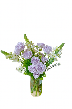 This elegant floral arrangement features delicate lavender roses paired with creamy white lisianthus and soft white snapdragons. Set in a tall, clear cylindrical glass vase, the bouquet is accented with lush green mossy fillers and sprigs of airy white limonium. The vertical orientation of the snapdragons and the pastel color palette create a graceful and serene aesthetic perfect for refined occasions.