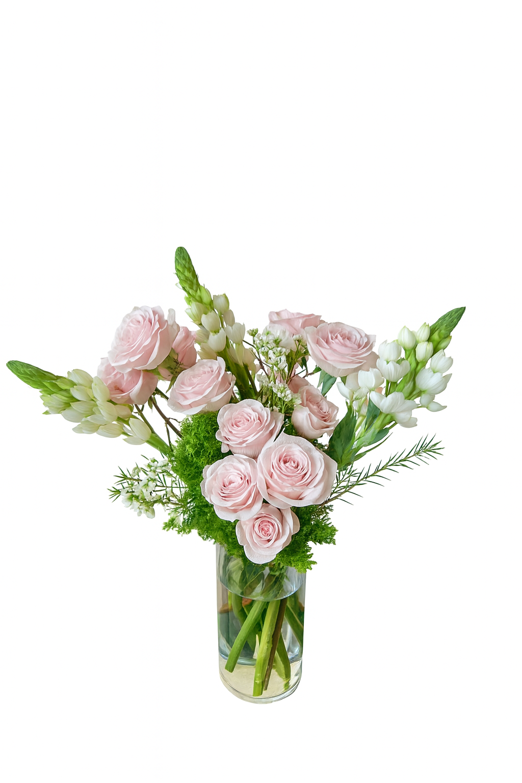 Elegant tall floral arrangement featuring soft blush pink roses, white bouvardia, green moss filler, and delicate white filler flowers. Designed in a clear cylindrical glass vase with submerged stems, this sophisticated piece exudes freshness and charm, perfect for romantic occasions or elegant corporate gifting.