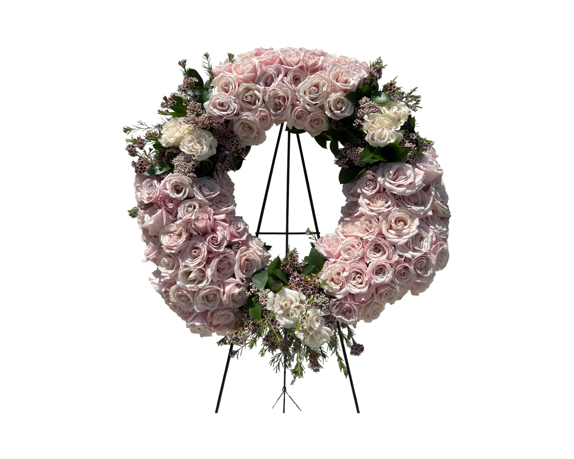 A sophisticated sympathy wreath displayed on a black metal easel, featuring a full ring of blush and ivory roses accented with light pink waxflower and soft greenery. This circular floral tribute conveys peace, remembrance, and eternal love—ideal for funeral services, memorials, or celebrations of life with a refined and gentle aesthetic.