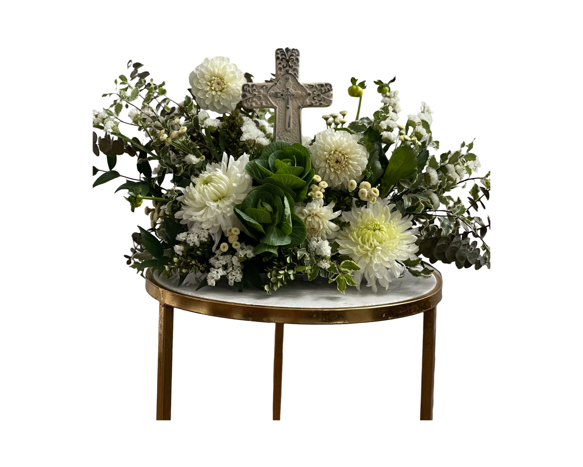 A reverent and nature-inspired floral arrangement featuring a stone cross at the center, surrounded by white dahlias, white chrysanthemums, ornamental green cabbage, white waxflower, button mums, eucalyptus, and lush foliage. Displayed on a marble table with gold trim, this elegant tribute is perfect for religious ceremonies, memorials, or moments of spiritual reflection.