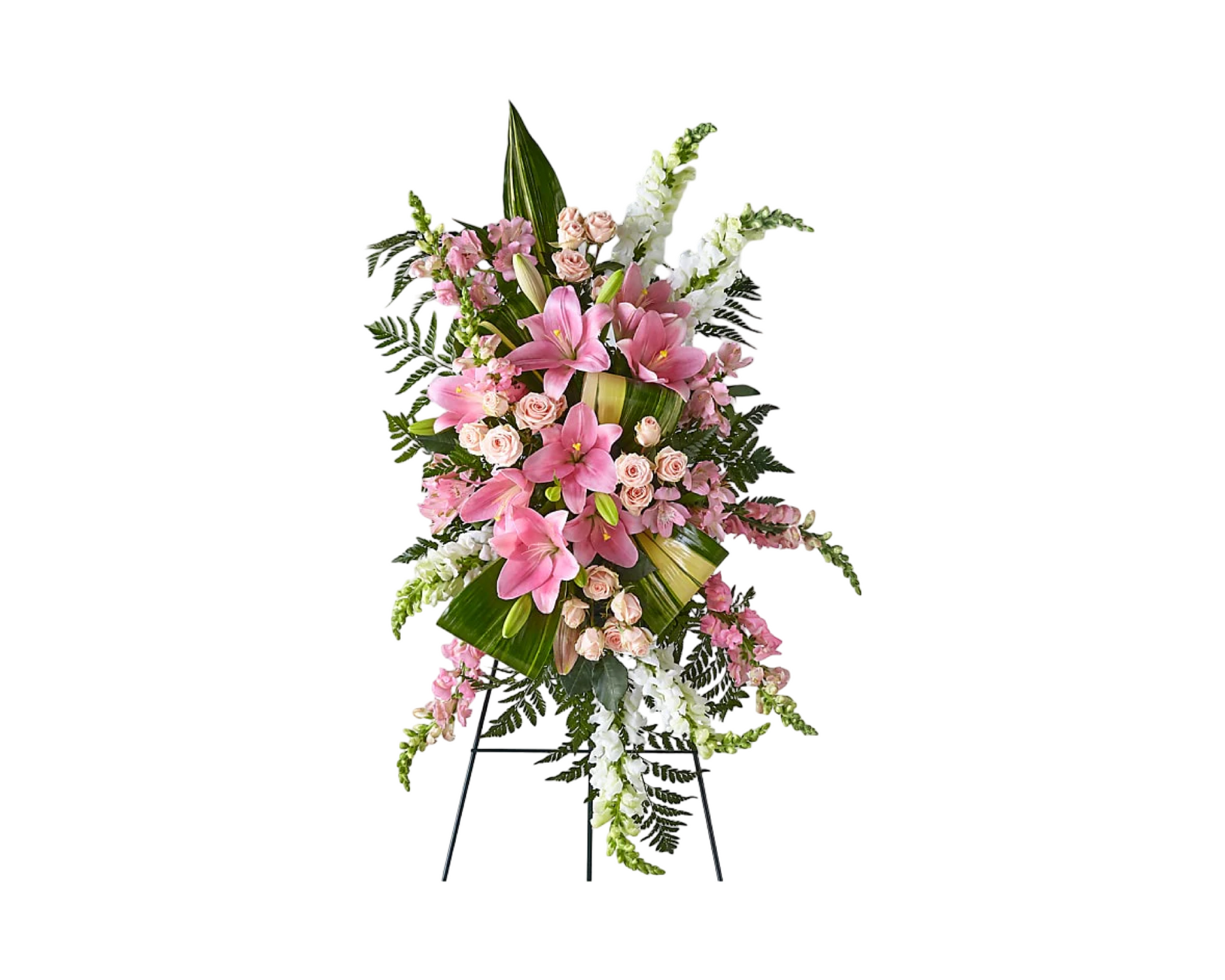 An elegant standing funeral spray displayed on a black easel, composed of pink lilies, soft blush spray roses, white snapdragons, and cascading ferns. Large tropical greens and folded ti leaves add structural contrast and depth. This tall and graceful floral tribute conveys heartfelt sympathy, support, and love—ideal for memorials, funerals, or celebrations of life.