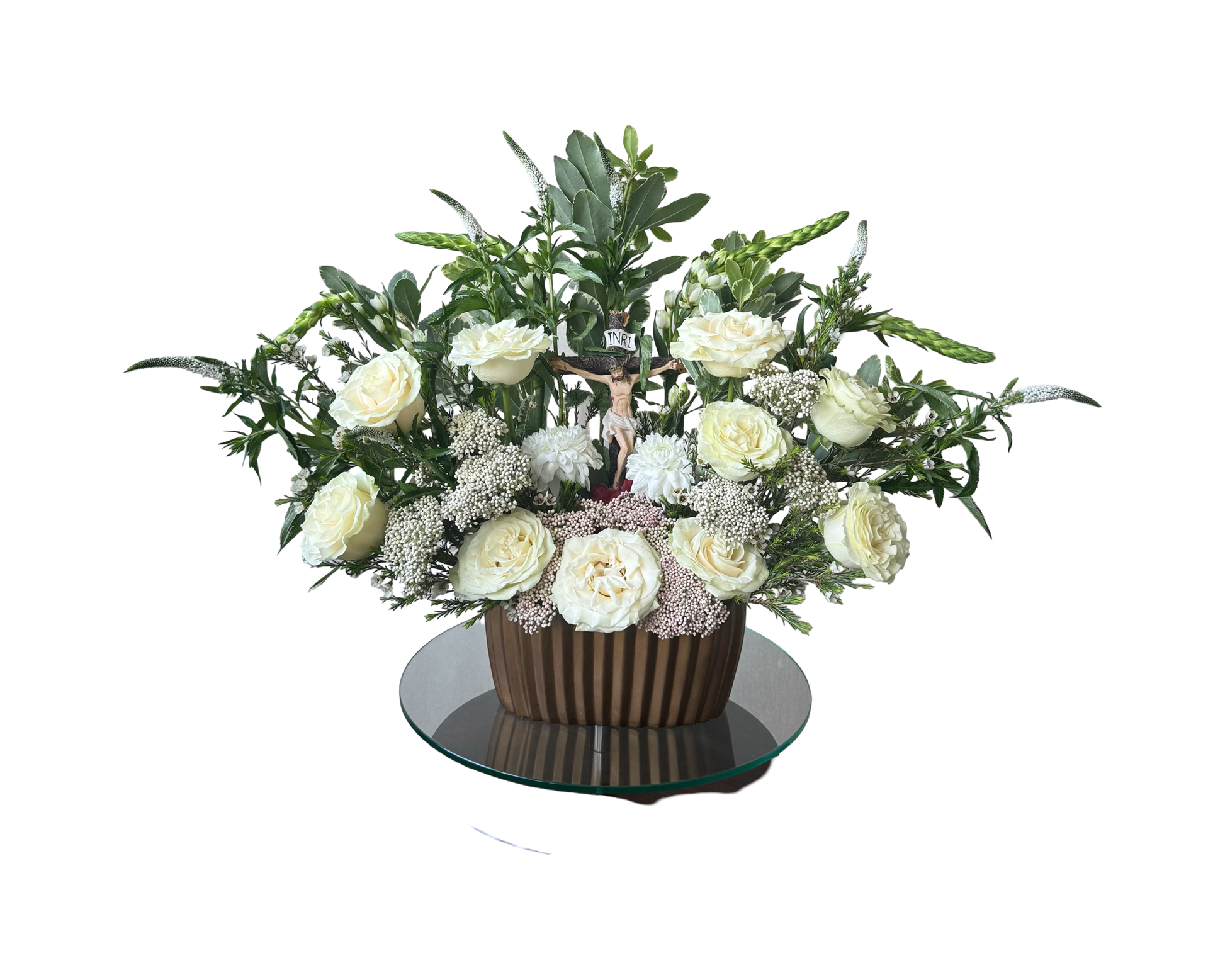 A sacred floral arrangement featuring a crucifix at the center, surrounded by ivory roses, white veronica, white dahlias, Queen Anne’s lace, and soft greenery. Arranged in a fluted dark bronze ceramic vase atop a glass pedestal, this design symbolizes faith, remembrance, and grace—perfect for funerals, religious services, or spiritual ceremonies.