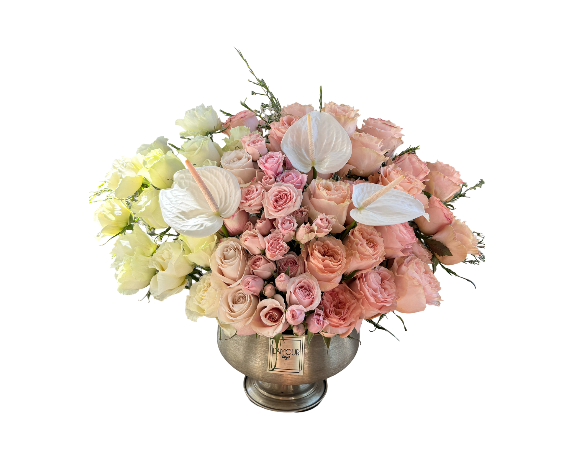 A sophisticated floral arrangement in a silver pedestal vase from L’amour Designs, featuring a soft palette of blush pink, ivory, and white. The bouquet includes blush roses, pink spray roses, white roses, and sculptural white anthurium flowers. This polished and refined design radiates luxury and serenity, perfect for upscale gifting and romantic gestures.