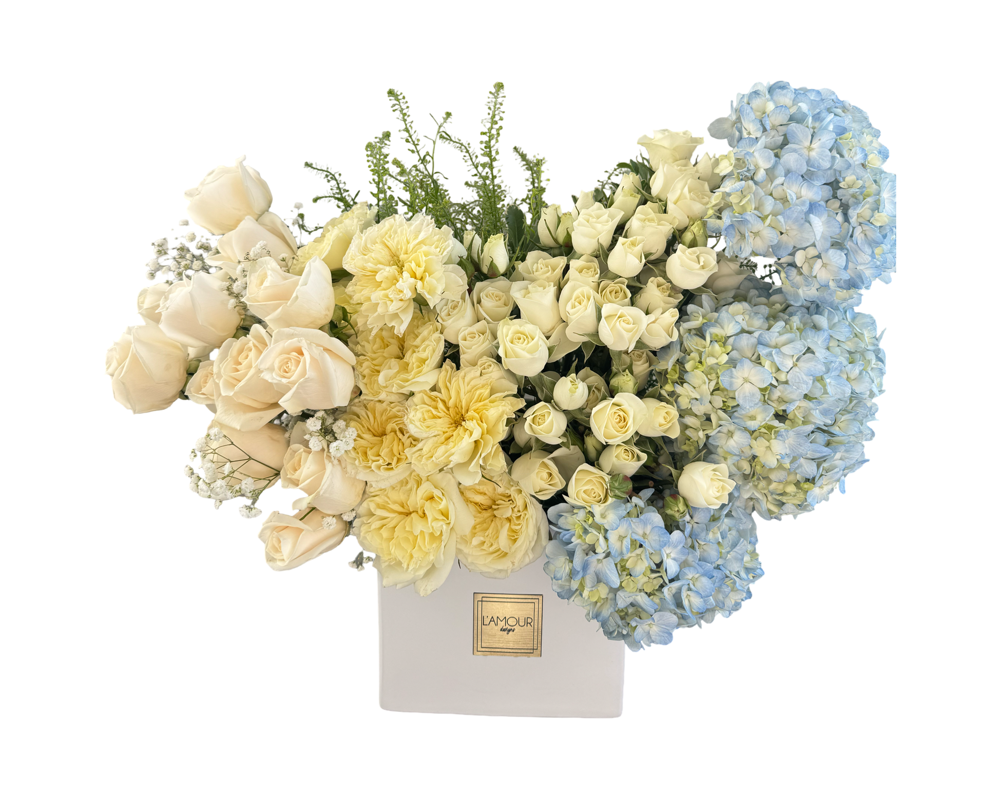 A grand and elegant floral arrangement in a white square L’amour Designs box, featuring ivory roses, cream spray roses, pale yellow garden roses, baby’s breath, and large light blue hydrangeas. The soft pastel palette creates a serene and refined look, ideal for sympathy, baby showers, weddings, or luxury gifting.