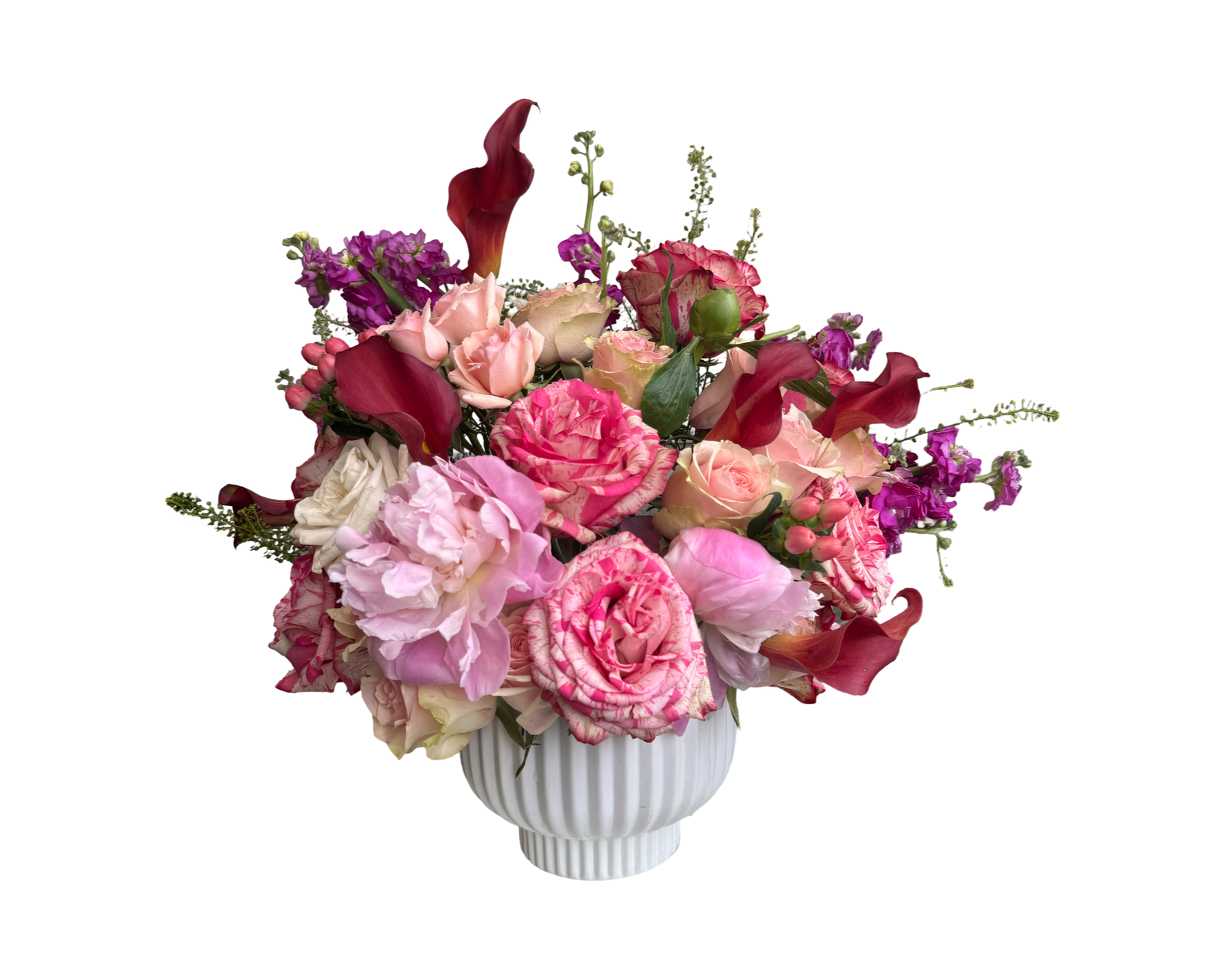 A bold and romantic floral arrangement featuring a luxurious mix of blush and hot pink roses, white roses, delicate spray roses, and lush pink peonies. Accents of red calla lilies, ruffled carnations, and purple stock flowers add depth and elegance. Displayed in a classic white ribbed vase, this arrangement is perfect for anniversaries, Valentine’s Day, birthdays, or Mother’s Day, making a striking and heartfelt statement of love and celebration.