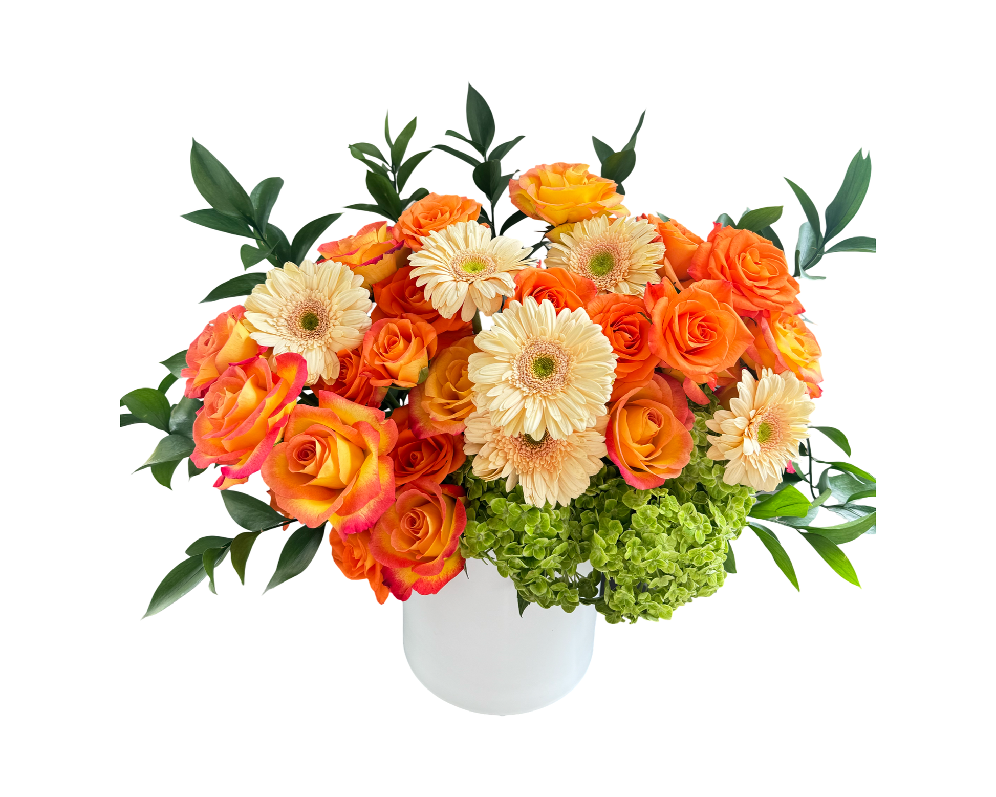 A radiant floral arrangement in a clean white vase featuring a vibrant mix of orange roses, peach gerbera daisies, green hydrangeas, and glossy green foliage. The energetic palette and structured dome shape make this bouquet a perfect choice for joyful celebrations, corporate gifting, and seasonal décor.