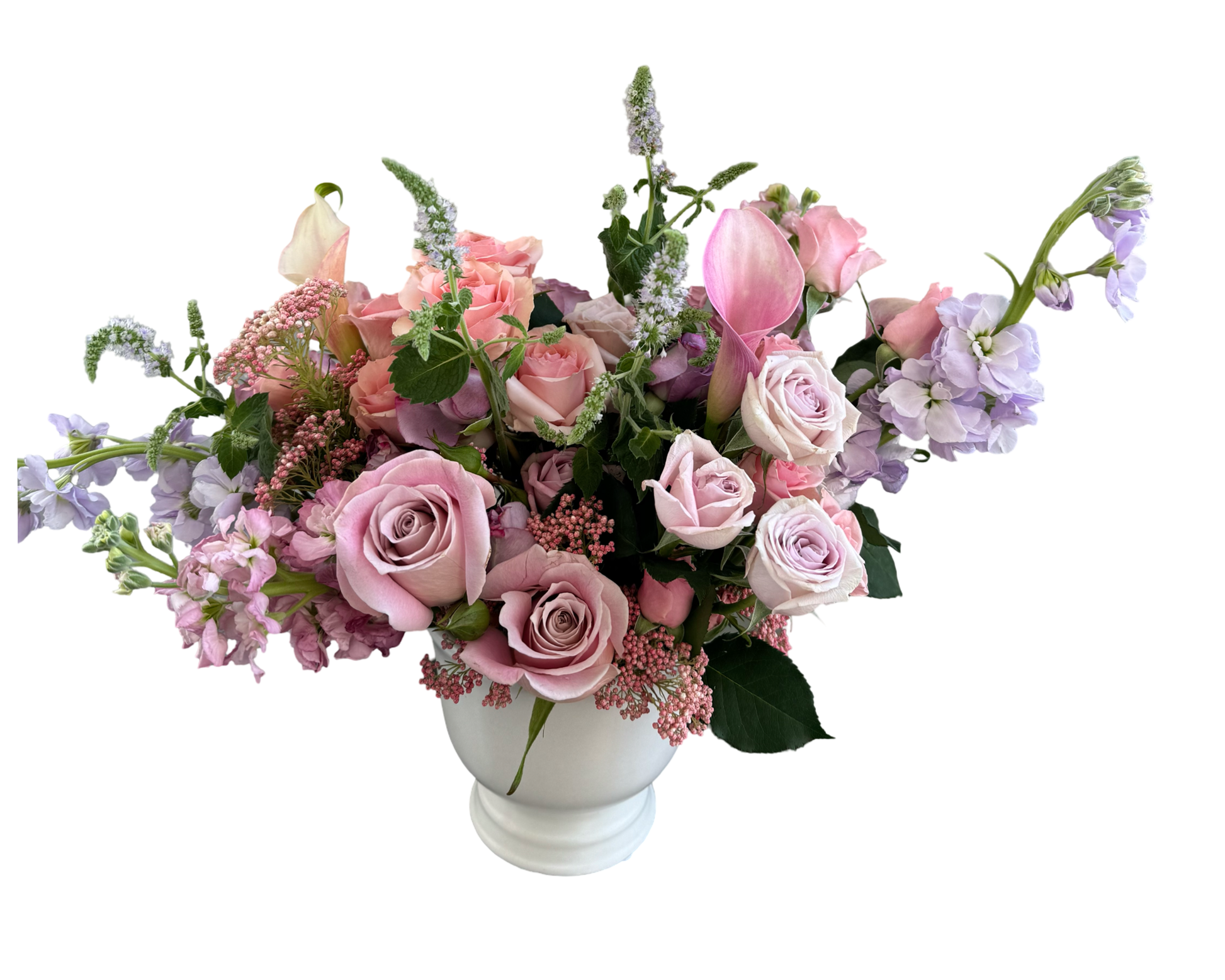 A romantic pastel floral arrangement in a soft white ceramic vase featuring a graceful mix of blush and lavender roses, pale peach calla lilies, lilac stock, and delicate pink rice flowers. The arrangement is thoughtfully designed with airy textures and flowing shapes, creating a gentle, elegant, and feminine presentation ideal for celebratory or intimate occasions.