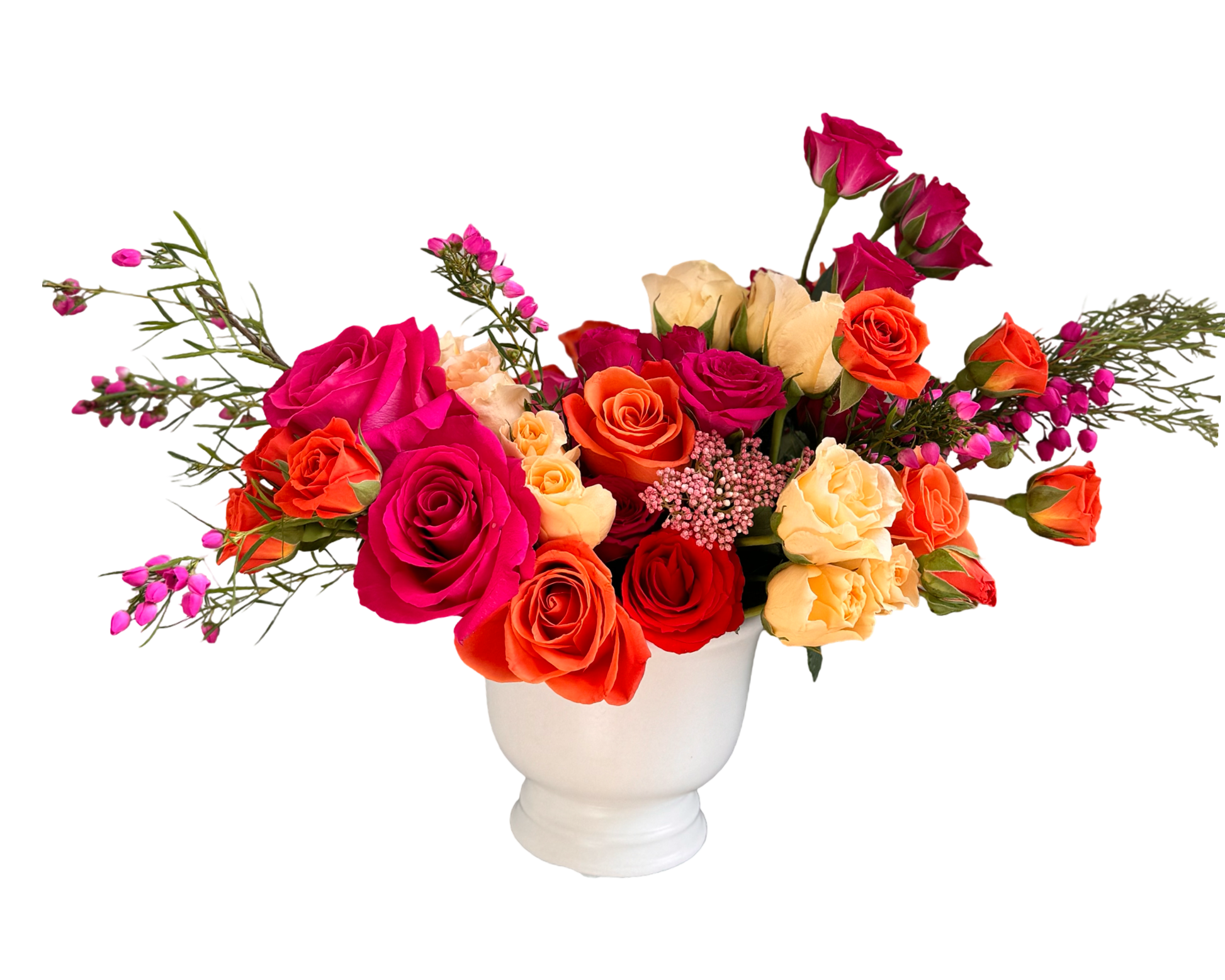 A striking and colorful floral arrangement in a white ceramic compote vase, featuring a vivid mix of fuchsia roses, orange roses, peach spray roses, red roses, and hot pink waxflower. The bright and cheerful palette creates a modern, celebratory look—perfect for festive occasions, warm thank-yous, and bold romantic gestures.