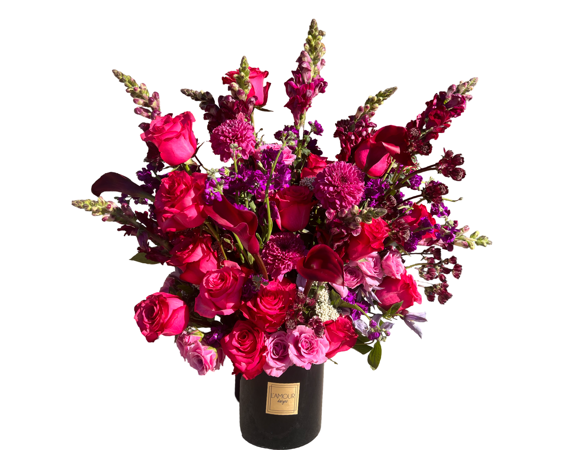 A dramatic and opulent floral arrangement in a tall black L’amour Designs vase, featuring a mix of hot pink roses, burgundy calla lilies, dark pink spray roses, magenta snapdragons, purple stock, and raspberry-hued chrysanthemums. The vibrant jewel tones and height create a luxurious statement perfect for upscale gifting and romantic celebrations.