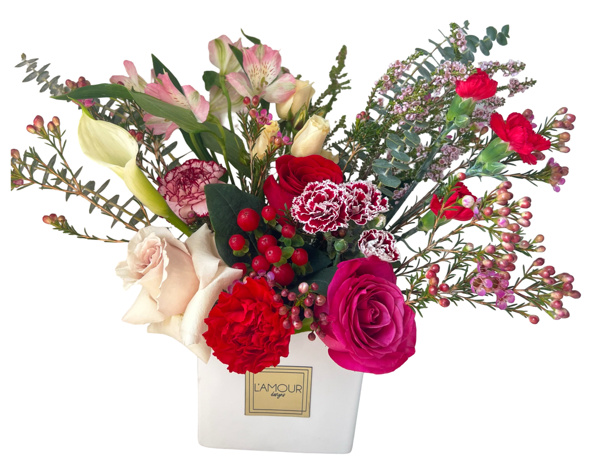 This floral arrangement features a romantic and textural mix of blooms presented in a square white L’amour hatbox. It includes vibrant red roses, hot pink roses, white calla lilies, light blush roses, and red carnations, paired with burgundy and white bicolor spray carnations, pink wax flowers, and red hypericum berries. The design is lush and elegant, with pops of bold red and pink accented by soft greenery and filler flowers for texture and volume.