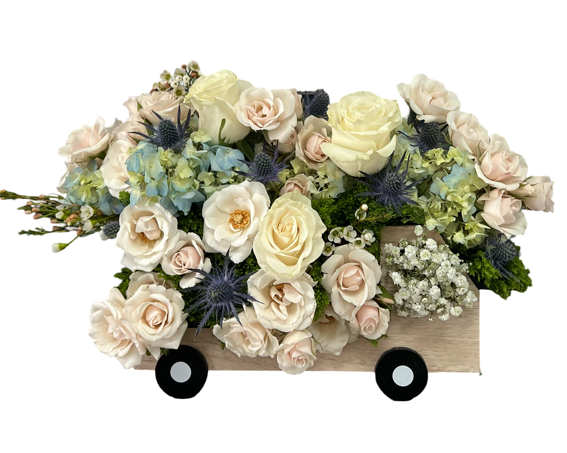 This whimsical and elegant floral design is arranged inside a wooden truck-shaped container, giving it a playful yet heartfelt touch. The bouquet features creamy ivory roses, blush spray roses, white ranunculus, pale blue hydrangeas, blue eryngium (thistle), wax flower, white baby’s breath, and soft green moss for texture. The gentle pastel tones combined with the unique presentation make this a charming choice for new beginnings, gentle condolences, or meaningful celebrations.