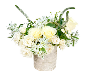 An elegant and serene floral arrangement featuring creamy white roses, delicate spray roses, and slender white veronica blooms. Accents of dusty miller, eucalyptus, and variegated greenery add texture and sophistication. Presented in a modern white textured vase, this arrangement exudes purity and grace, making it perfect for anniversaries, sympathy gestures, memorial services, or sophisticated home décor.
