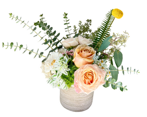A charming floral arrangement in a textured taupe ceramic pot, featuring peach and cream roses, yellow craspedia (billy ball), white cosmos, chamomile, green moss, and assorted eucalyptus and ferns. With its organic shape and neutral palette, this design is ideal for rustic weddings, thoughtful gifts, or springtime celebrations.