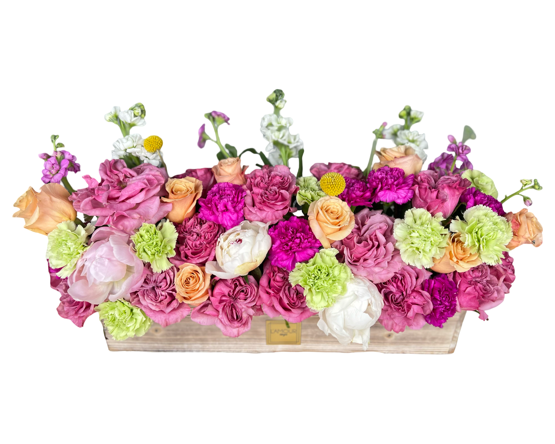 A joyful rectangular floral arrangement in a whitewashed wooden box by L’amour Designs, filled with a lush mix of lavender lisianthus, peach roses, white peonies, bright green carnations, hot pink carnations, lavender roses, white stock, and yellow craspedia. The lively blend of pastels and brights makes it perfect for spring celebrations, festive occasions, and cheerful gifting.