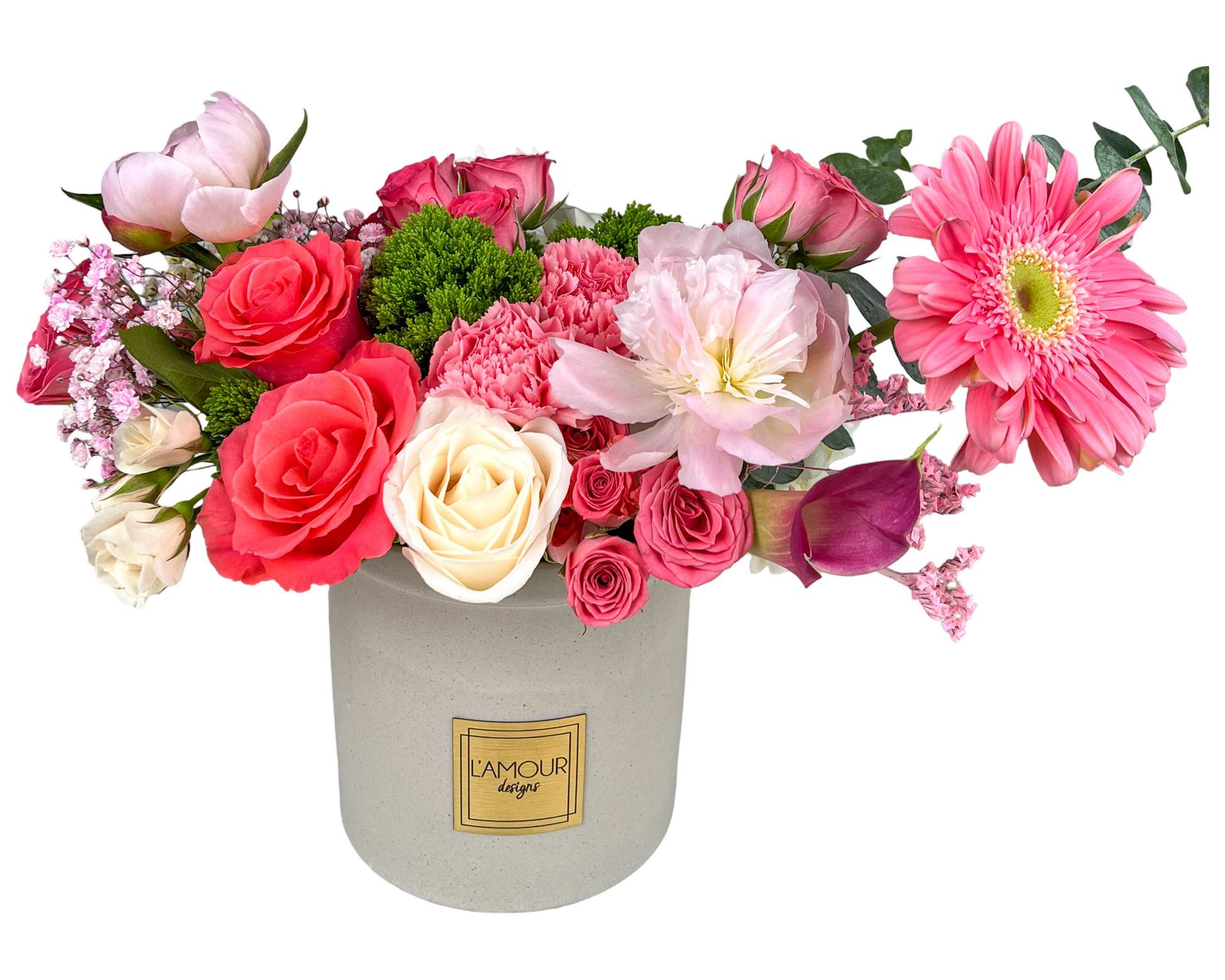 This floral arrangement features a vibrant mix of pink and fuchsia blooms in a light gray ceramic vase labeled "L’Amour Designs." It includes vivid hot pink gerbera daisies, soft pink peonies, classic pink and cream roses, calla lilies, carnations, tulips, and baby’s breath, creating a lush and romantic display. The contrasting textures of the various blooms and soft greenery add visual interest and dimension, making it a cheerful and charming bouquet perfect for celebrations or heartfelt gestures.