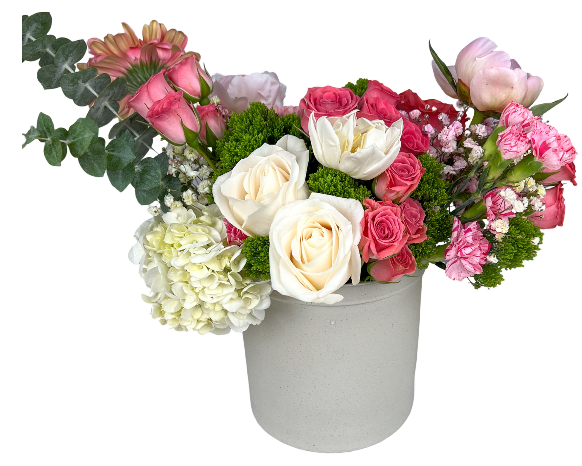 A charming pastel floral arrangement presented in a matte off-white ceramic vase, featuring ivory roses, white tulips, pale green hydrangeas, blush peonies, pink gerbera daisies, pink carnations, spray roses, baby’s breath, and pops of green moss filler and eucalyptus. This design blends elegance and freshness—perfect for romantic gestures, spring celebrations, or heartfelt messages of love and support.