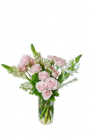Elegant tall floral arrangement featuring soft blush pink roses, white bouvardia, green moss filler, and delicate white filler flowers. Designed in a clear cylindrical glass vase with submerged stems, this sophisticated piece exudes freshness and charm, perfect for romantic occasions or elegant corporate gifting.