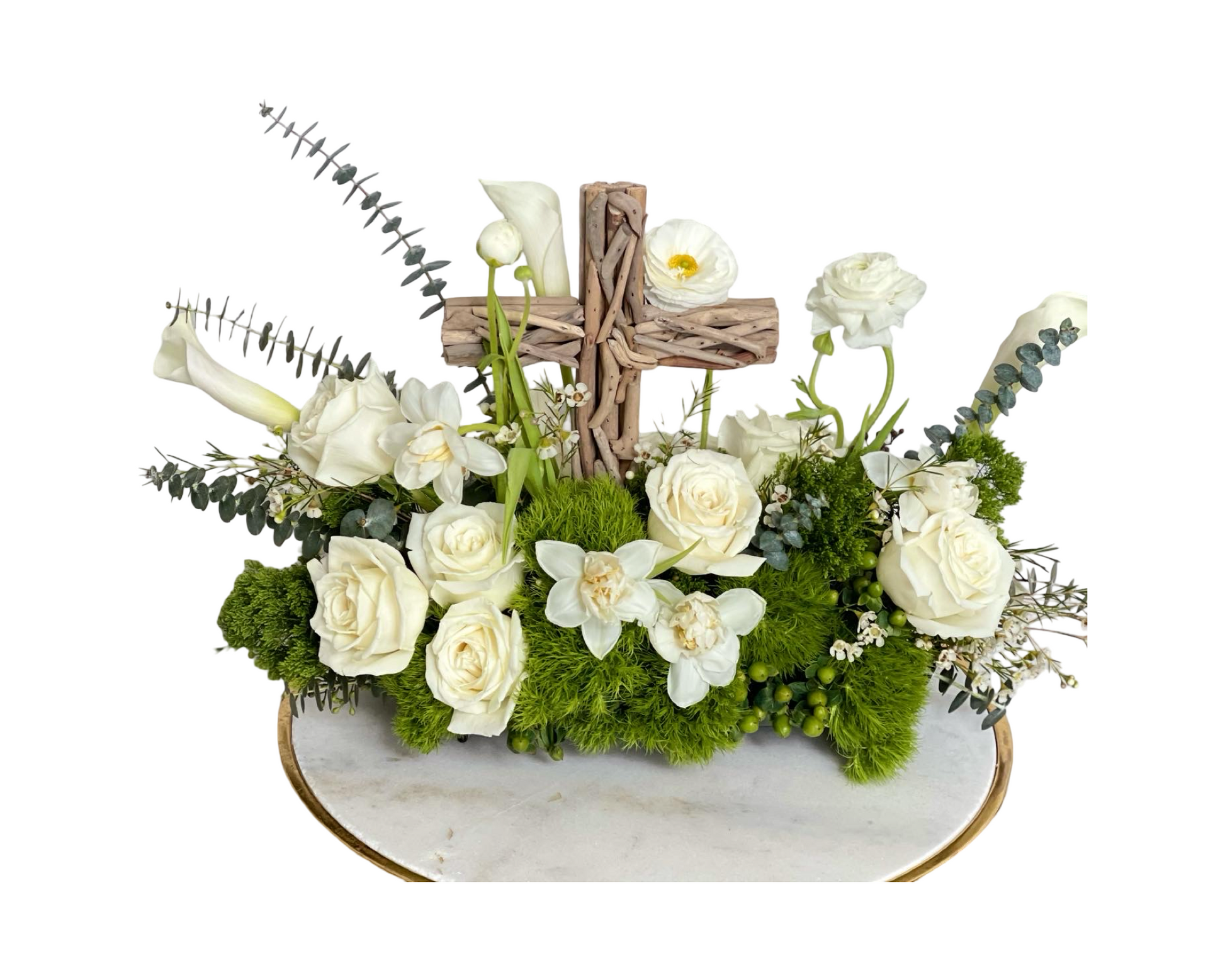 A serene religious-themed sympathy arrangement displayed on a marble base with gold trim. Featuring a rustic wooden cross at the center, it is surrounded by white roses, calla lilies, orchids, anemones, and lush green moss with eucalyptus accents. A beautiful tribute for memorial services, baptisms, and spiritual occasions.