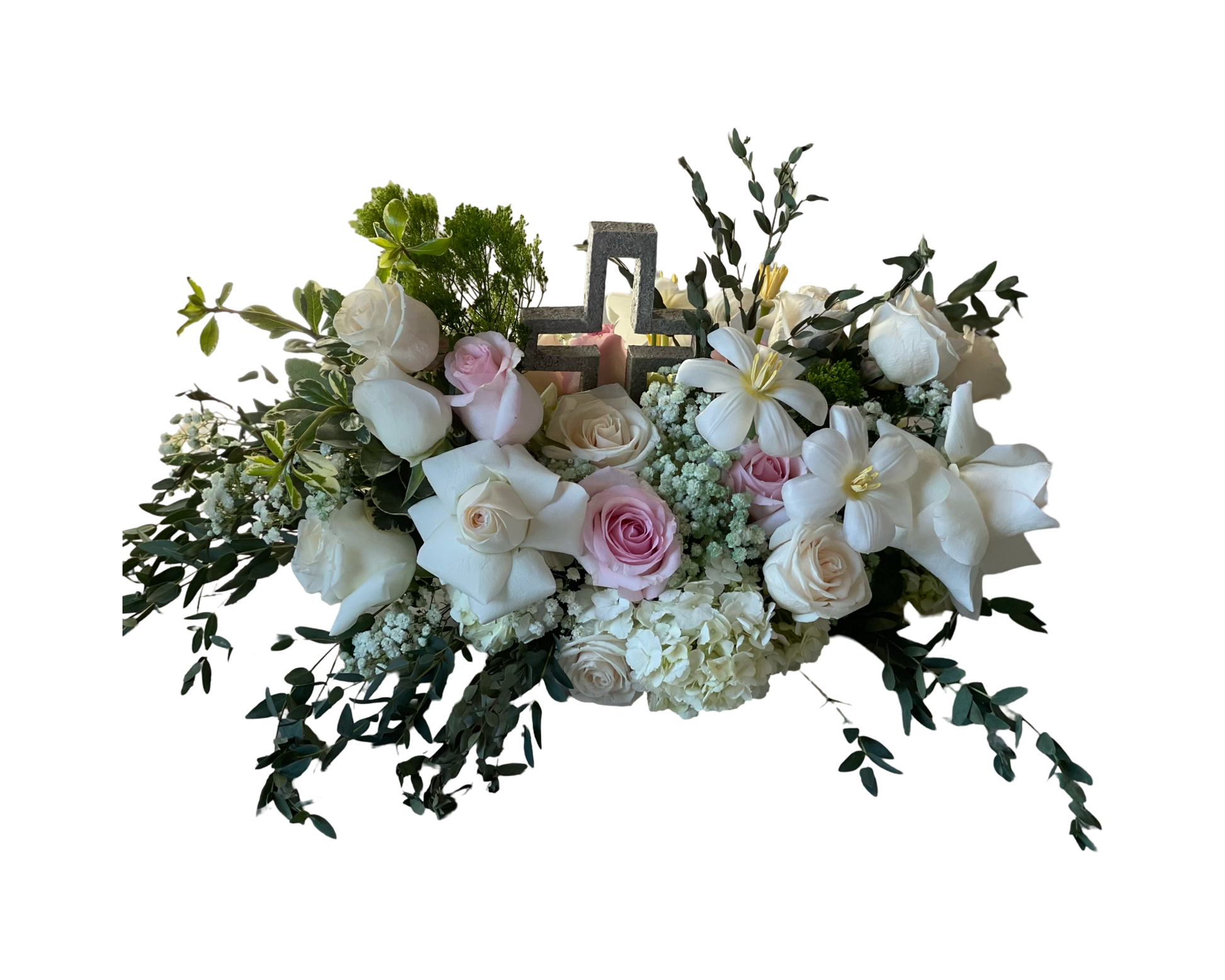 A soft and serene floral arrangement centered around a stone cross, featuring white and blush roses, white lilies, baby’s breath, white hydrangeas, light pink roses, and assorted greenery. This elegant, pastel-toned piece is ideal for sympathy, religious ceremonies, and moments of spiritual reflection.