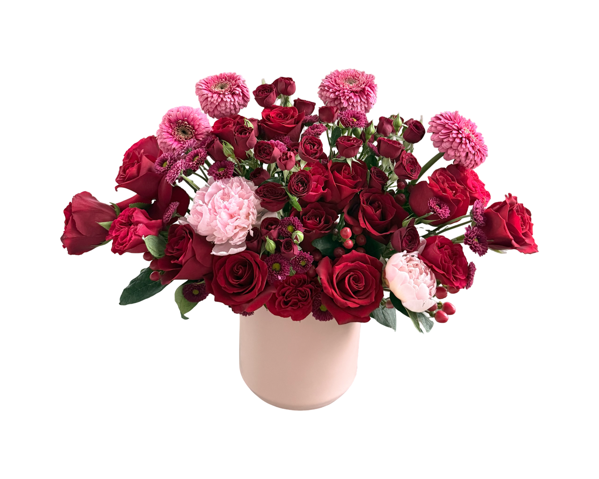 A lush floral arrangement in a soft blush ceramic vase, featuring a mix of red roses, pink chrysanthemums, pink peonies, red spray roses, and burgundy button mums. The deep romantic tones contrasted with light pink accents create an elegant and passionate bouquet, perfect for heartfelt gifting and special romantic moments.