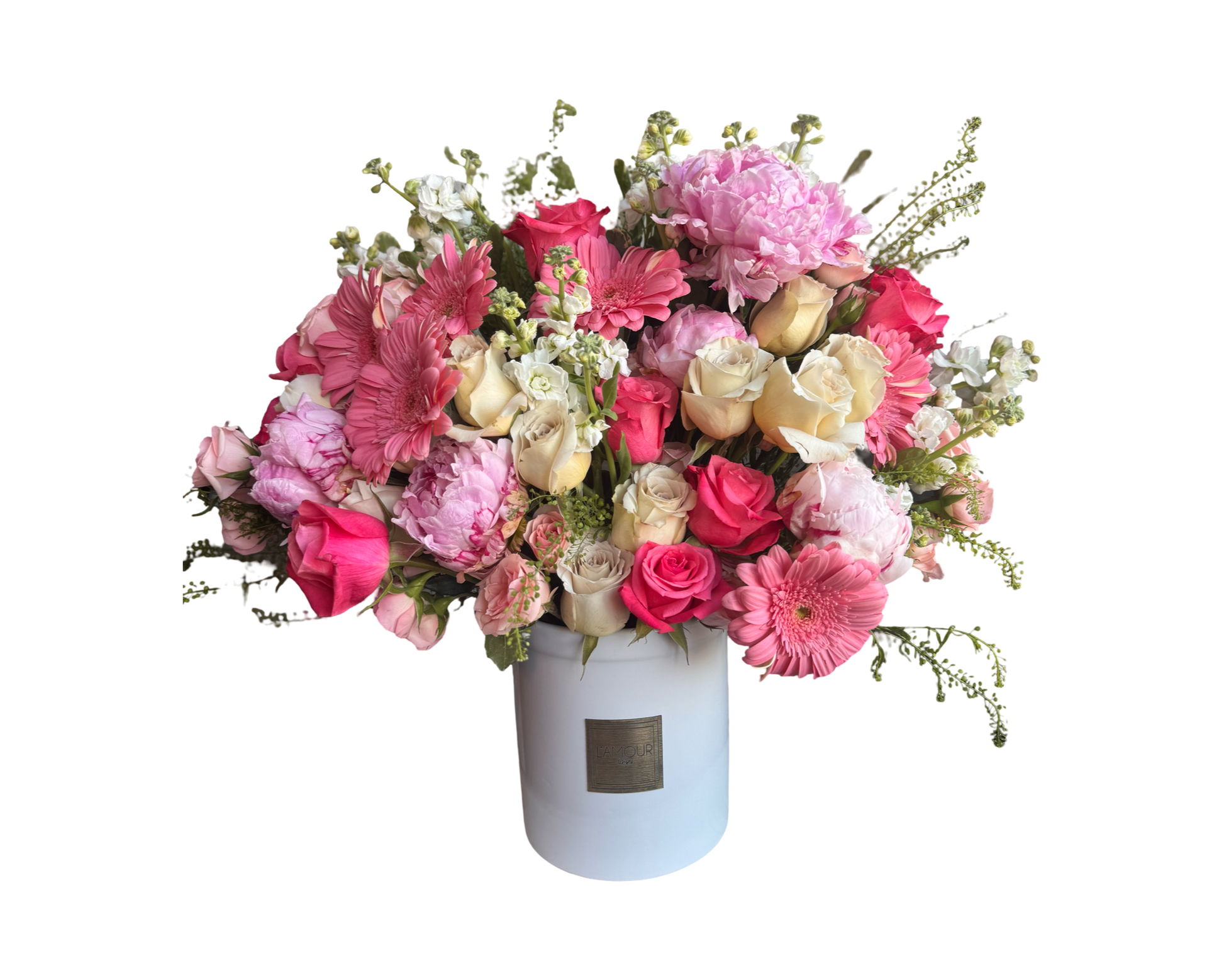 A generous, pastel-toned floral arrangement in a white cylindrical L’amour Floral Designs hatbox, overflowing with soft pink and ivory blooms. The bouquet features pink peonies, ivory and blush roses, coral spray roses, pink gerbera daisies, white stock, and assorted seasonal greenery. This elegant and dreamy arrangement is ideal for romantic celebrations, heartfelt milestones, and feminine gifting occasions.