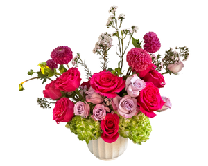 This floral arrangement bursts with romantic vibrancy, featuring hot pink roses, lavender roses, green hydrangeas, pink pompom chrysanthemums, and delicate sprigs of white filler flowers. Set in a soft white ceramic vase, the design combines lush textures with a bold color palette of hot pink, soft lavender, and lime green. The overall aesthetic is joyful and energetic—ideal for making a bright and heartfelt statement.