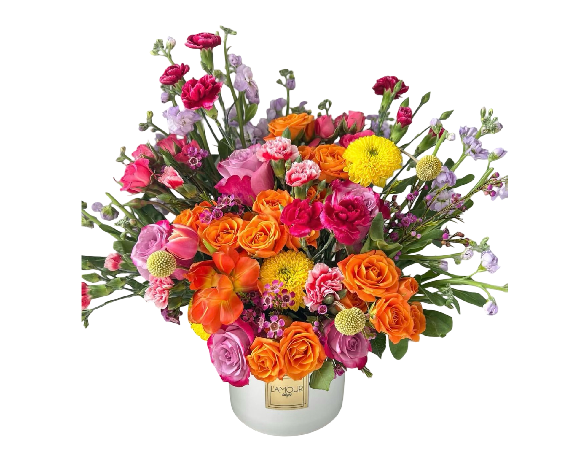 A vibrant and joyful floral arrangement in a white ceramic vase from L’amour Designs, showcasing a lively mix of orange roses, yellow pompom chrysanthemums, pink carnations, hot pink spray roses, purple stock, lavender lisianthus, yellow craspedia, and orange ranunculus. This colorful bouquet radiates happiness and energy—perfect for celebrations, birthdays, and uplifting gifts.