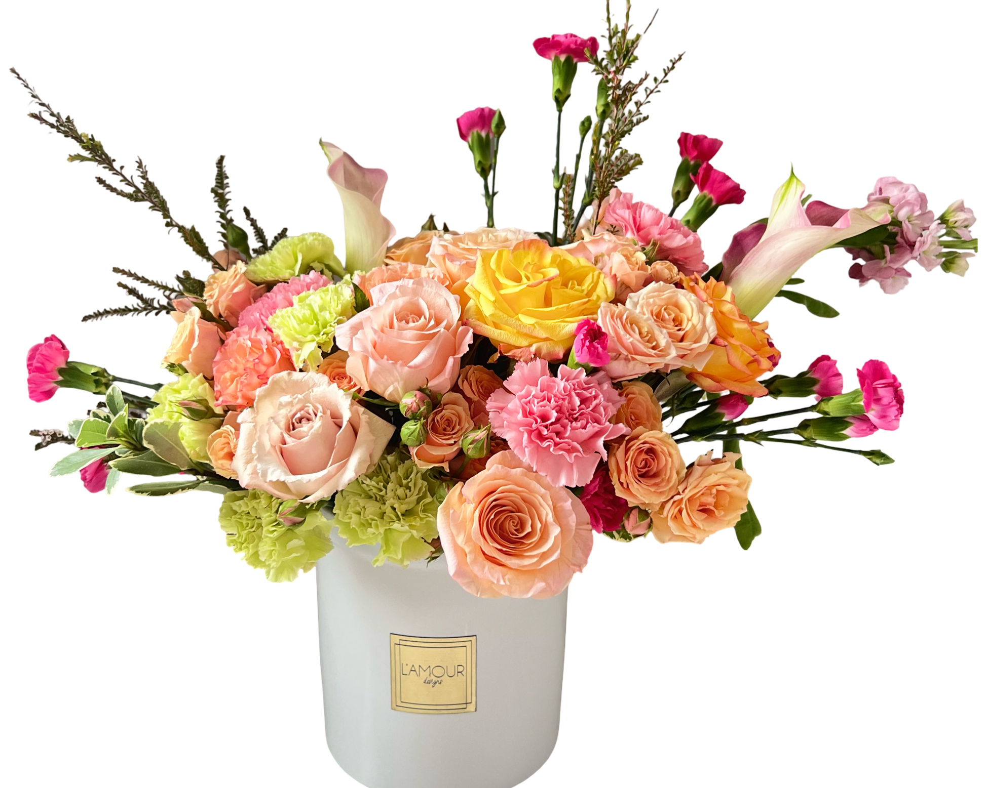 A bright and cheerful floral arrangement featuring sunny yellow roses, peach and blush roses, delicate pink spray roses, vibrant pink carnations, and fresh green carnations. Elegant pink calla lilies and soft stock flowers add height and texture, while sprigs of greenery bring balance to the design. Presented in a chic white L'amour Floral Designs vase, this arrangement is perfect for birthdays, anniversaries, Mother’s Day, or as a joyful gift to brighten someone’s day.