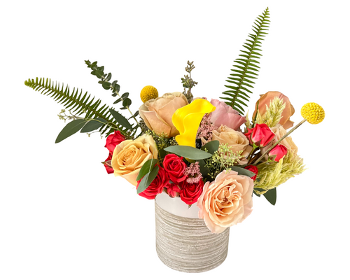 Amber Flame floral arrangement with golden roses, yellow calla lilies, and greenery in a ribbed tan ceramic vase.