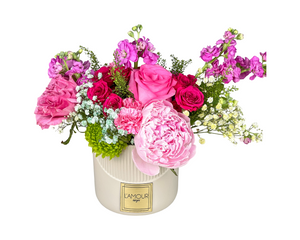 A vibrant and romantic floral arrangement featuring hot pink roses, lush pink peonies, spray roses, and pink carnations. Accents of lavender stock flowers, delicate baby’s breath, and bright green chrysanthemums add contrast and texture. Presented in a modern white vase with the L'amour Floral Designs label, this arrangement is perfect for anniversaries, birthdays, Mother’s Day, or as a colorful statement piece for any celebration.