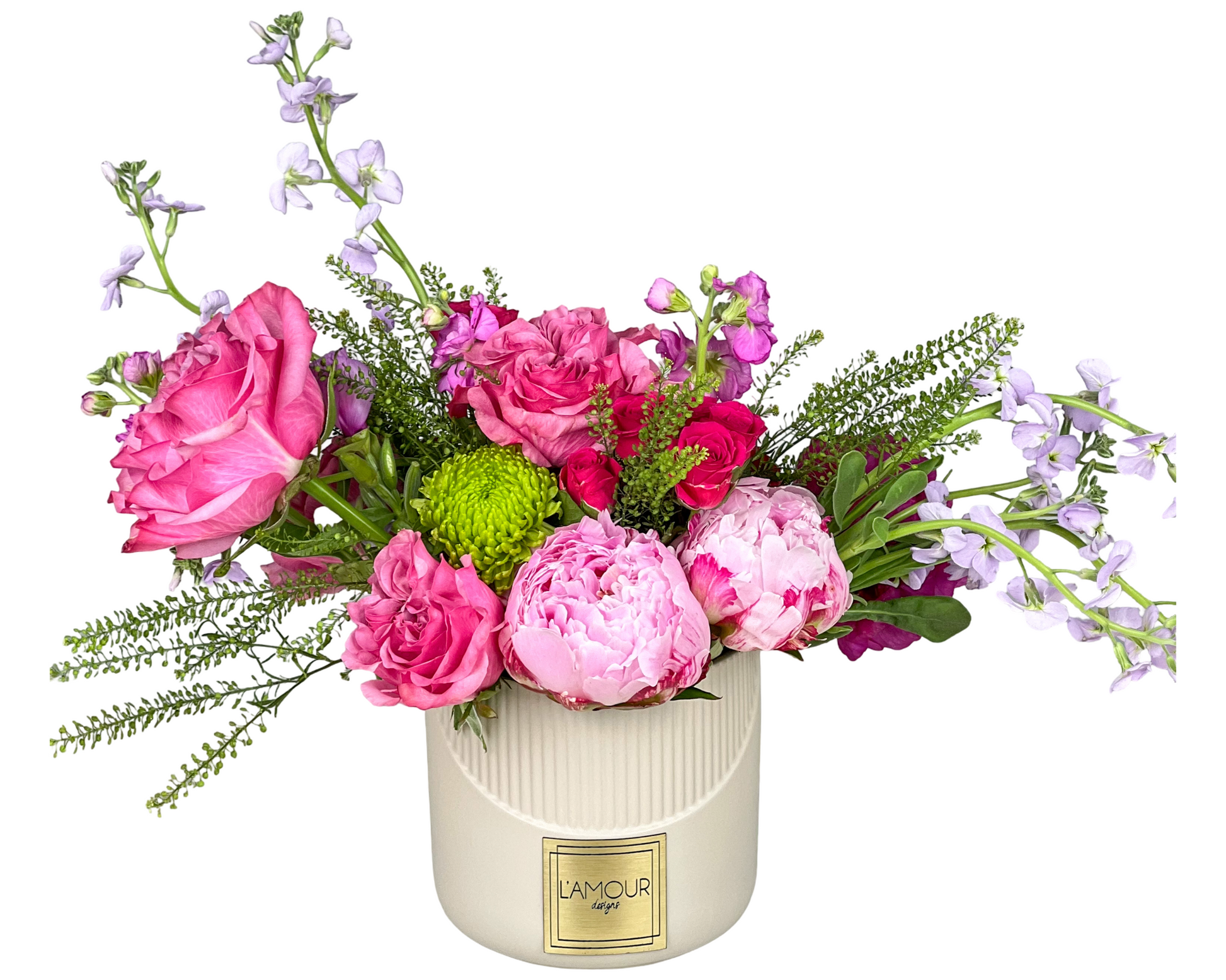 A romantic garden-inspired arrangement in a ribbed cream ceramic vase from L’amour Designs, featuring pink roses, peonies, spray roses, bright green button chrysanthemums, lavender stock, and assorted greens. The vibrant mix of textures and tones makes it perfect for celebratory moments, spring gifting, or romantic gestures.