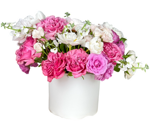A soft and romantic floral arrangement featuring lush pink roses, delicate garden roses, and creamy white tulips. Blush spray roses, lisianthus, and stock flowers add texture and fullness to the design. Presented in a sleek white vase, this pastel-toned arrangement exudes elegance and grace, making it ideal for anniversaries, birthdays, Mother’s Day, or Valentine’s Day celebrations.