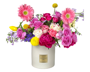 A cheerful and colorful floral arrangement featuring a lively mix of hot pink peonies, soft pink roses, playful pink gerbera daisies, and delicate carnations. Accents of yellow tulips, bright yellow craspedia, and purple statice add vibrant contrast, while touches of greenery balance the design. Presented in a modern white vase with the L'amour Floral Designs label, this arrangement is perfect for birthdays, anniversaries, Mother’s Day, or any joyful celebration.